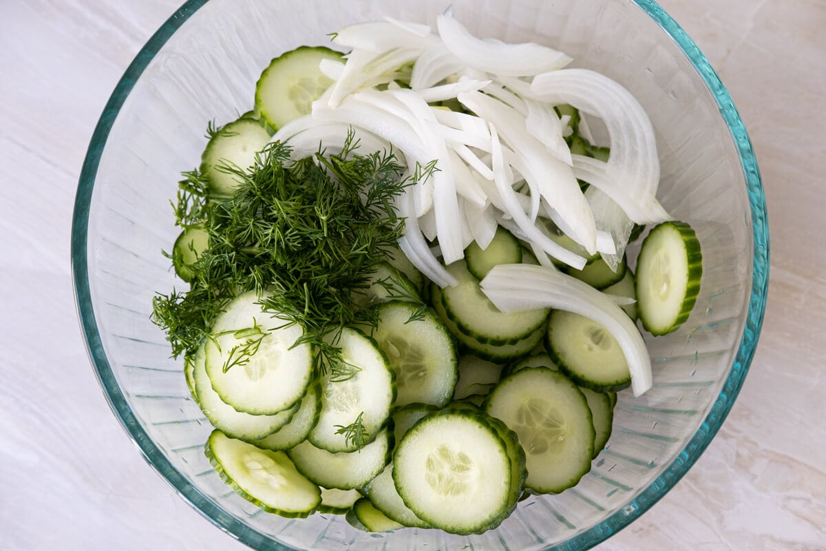 Sliced cucumbers, sliced onion and chop fresh dill in a bowl.