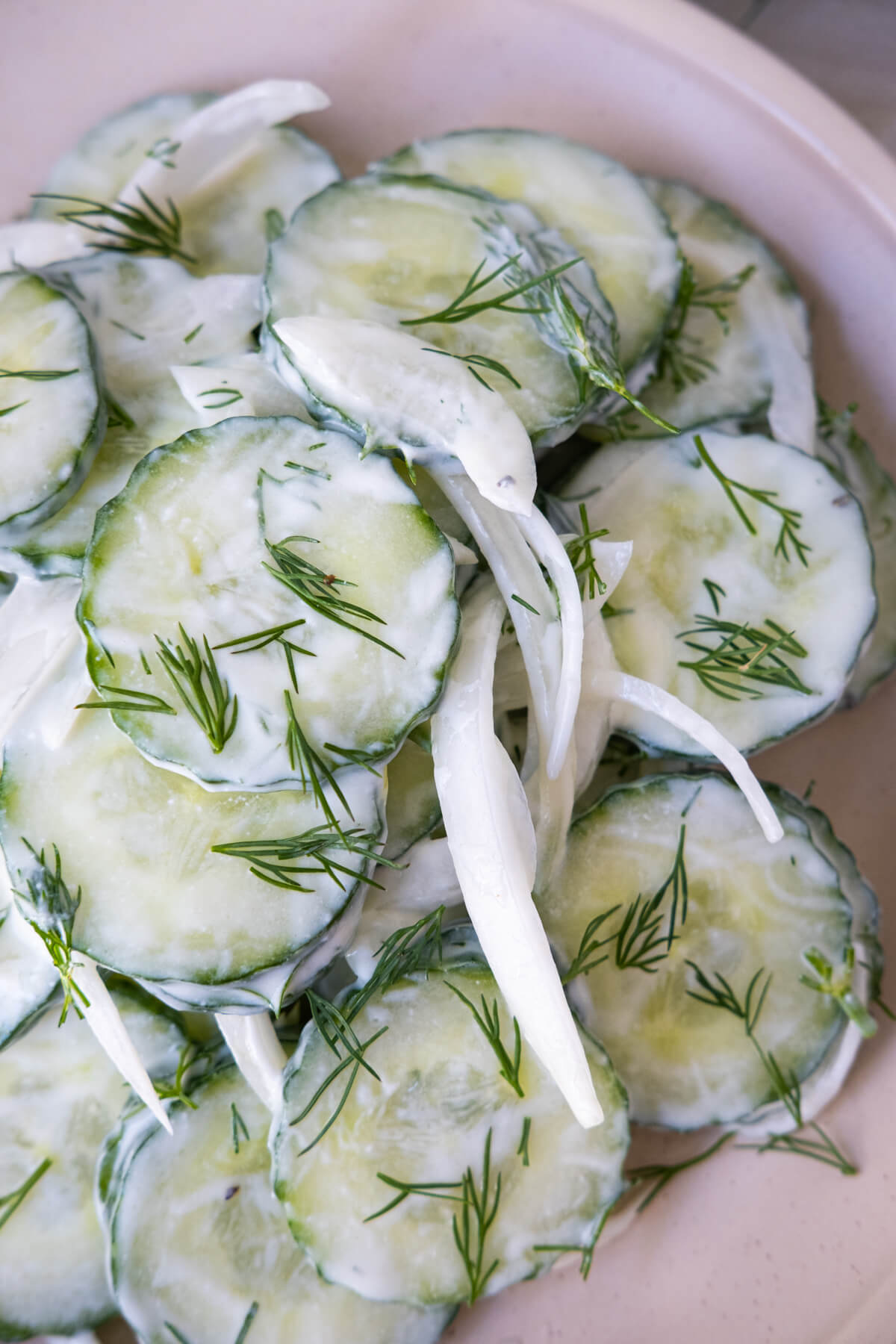 Creamy cucumber salad with white onion slices on a white plate garnished with chopped dill. 