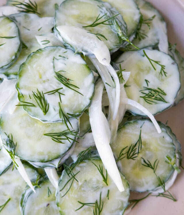 Creamy cucumber salad with white onion slices on a white plate garnished with chopped dill.