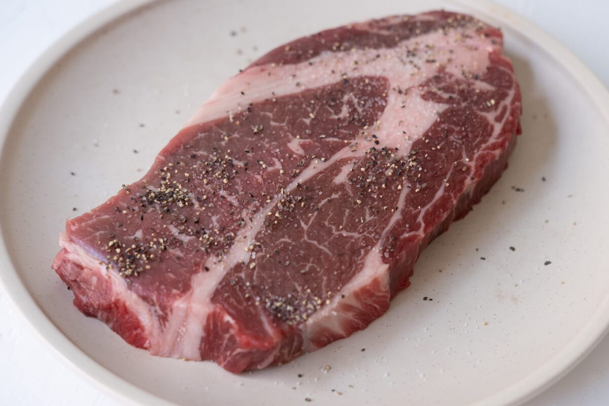 Wagyu beef seasoned with salt and ground black pepper on a plate.