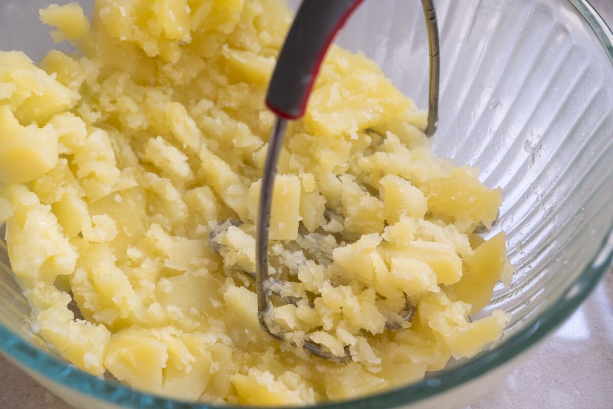 Potatoes being gently mashed in a bowl. 