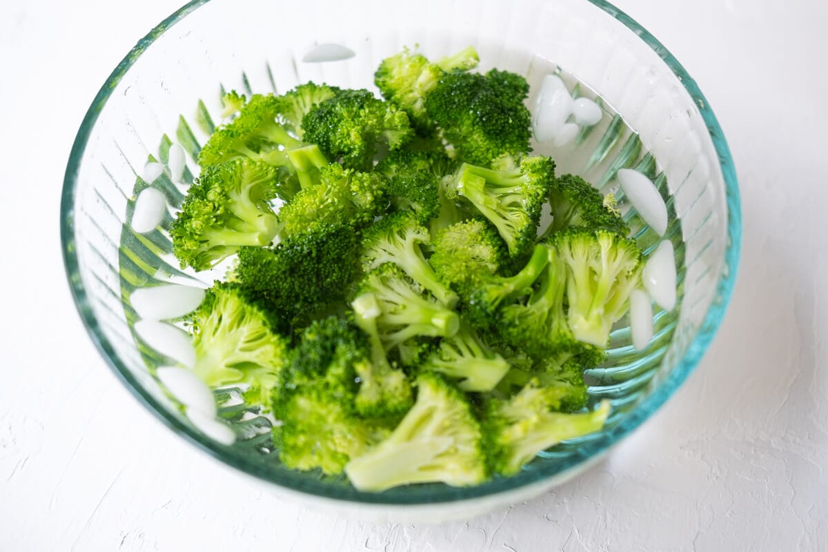 Boiled broccoli sitting in ice-cold water in a bowl. 