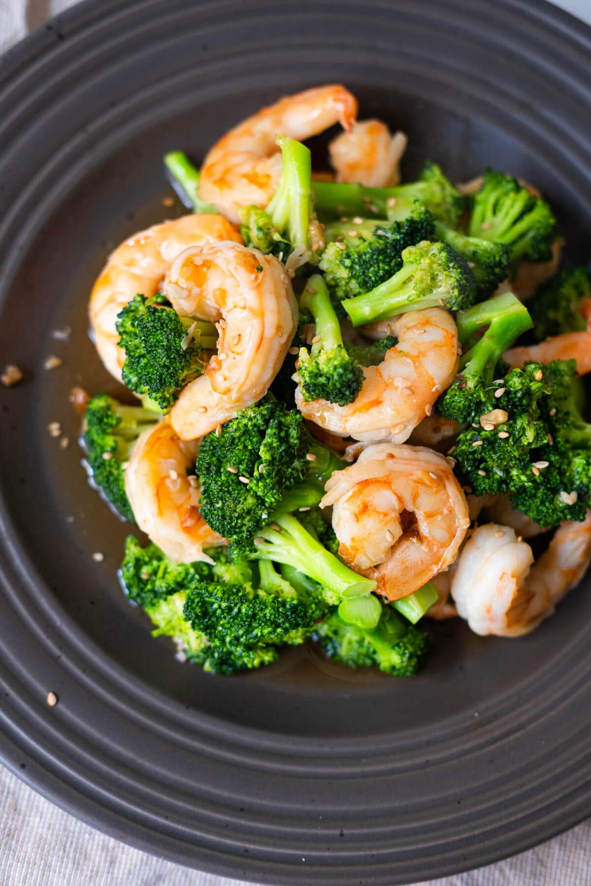 Shrimp and broccoli coated with brown sauce and served in a large black shallow plate. 