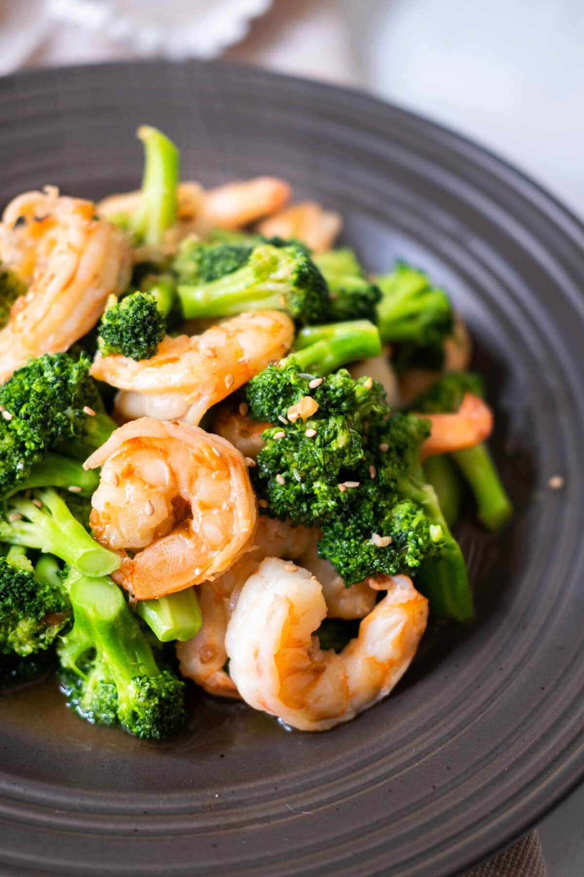 Healthy stir-fried broccoli and shrimps served hot with white sesame seeds on top and a napkin placed behind it.