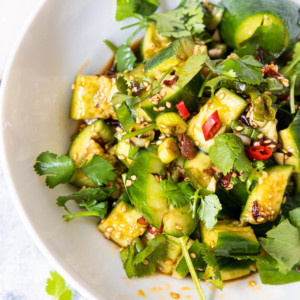 A bowl of smashed cucumber salad with sesame seeds, chopped red pepper and cilantro sprinkled on top.