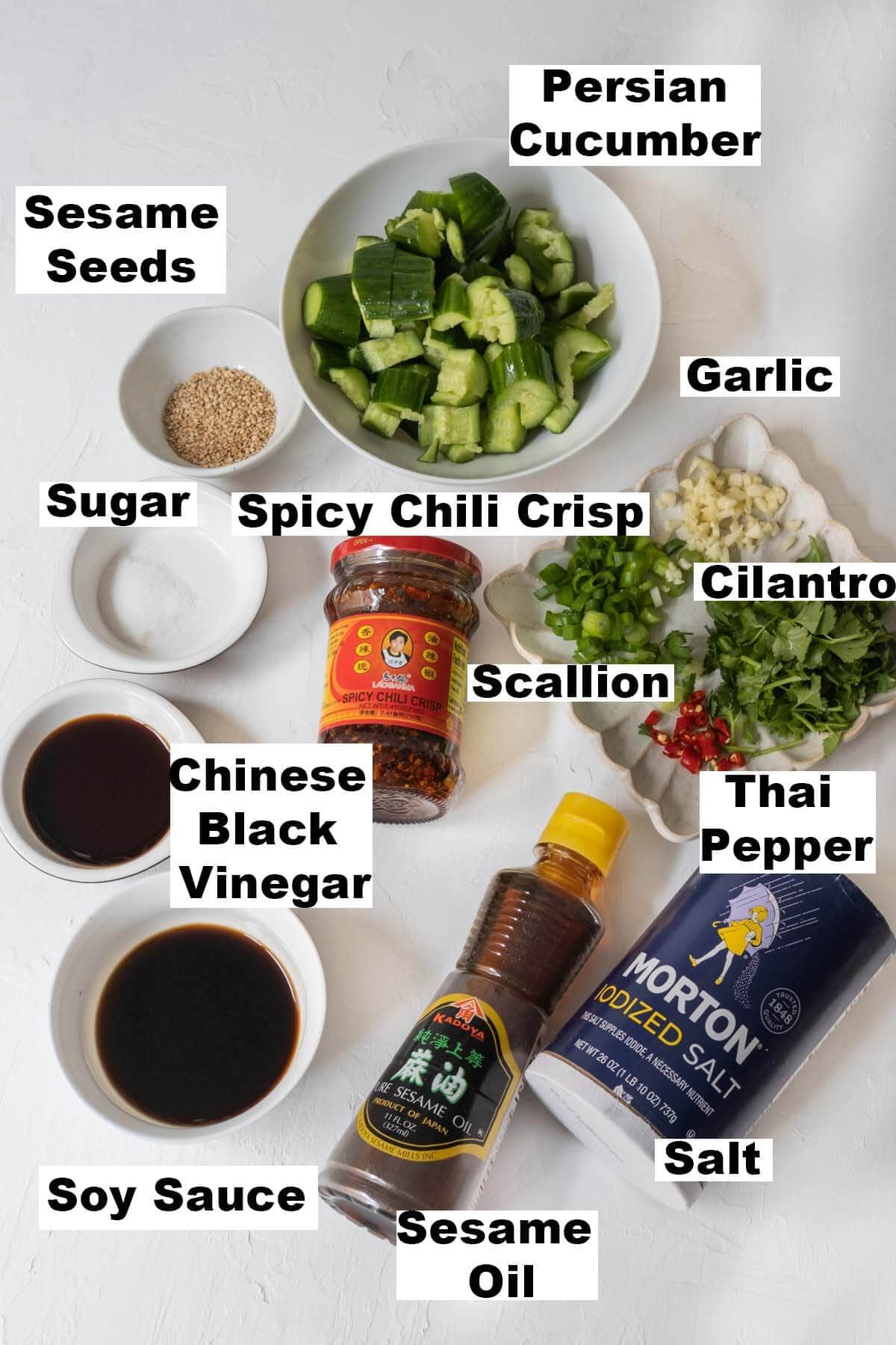 Smashed cucumber salad ingredients: Persian cucumber, sesame seeds, garlic, sugar, spicy chili crisp, scallion, cilantro, Chinese black vinegar, soy sauce, sesame oil and salt. 