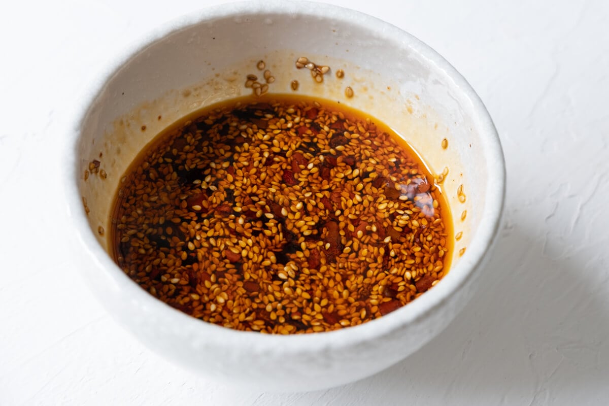 A small bowl of dressing with white sesame seeds and spicy chili crisps on top. 