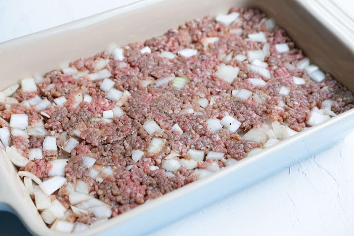 Marinaded beef and diced onion laid in rectangle baking pan. 