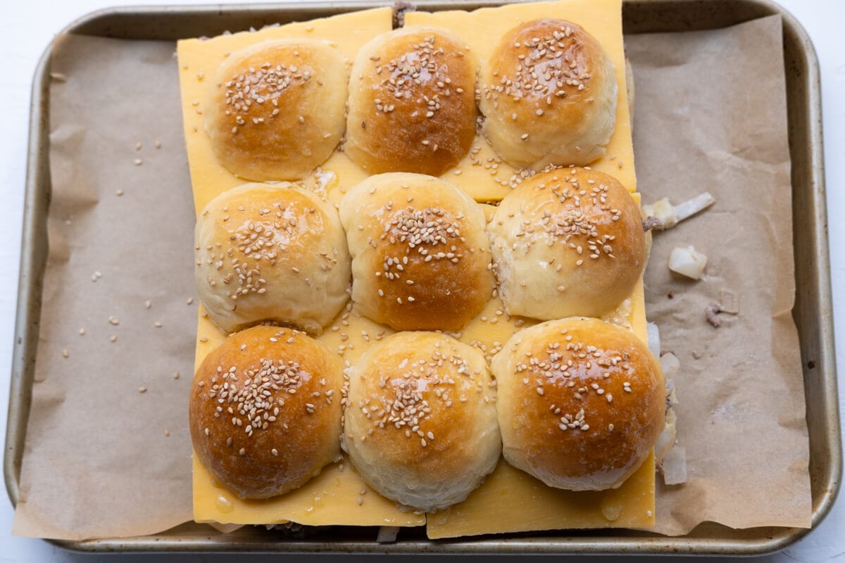 Assembled sliced buns, baked beef, cheese slices and sprinkle with white sesame seeds on top on a oven tray. 
