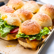 Cheeseburger sliders placed on a baking sheet lined with parchment paper.