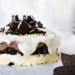 Ice cream cake topped with Oreo crumbs and sprinkles with whipped cream drizzle down the side.