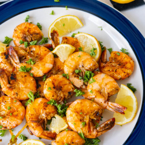 Old Bay shrimp served with lemon wedges and chopped parsley and with with half cut lemon aside.