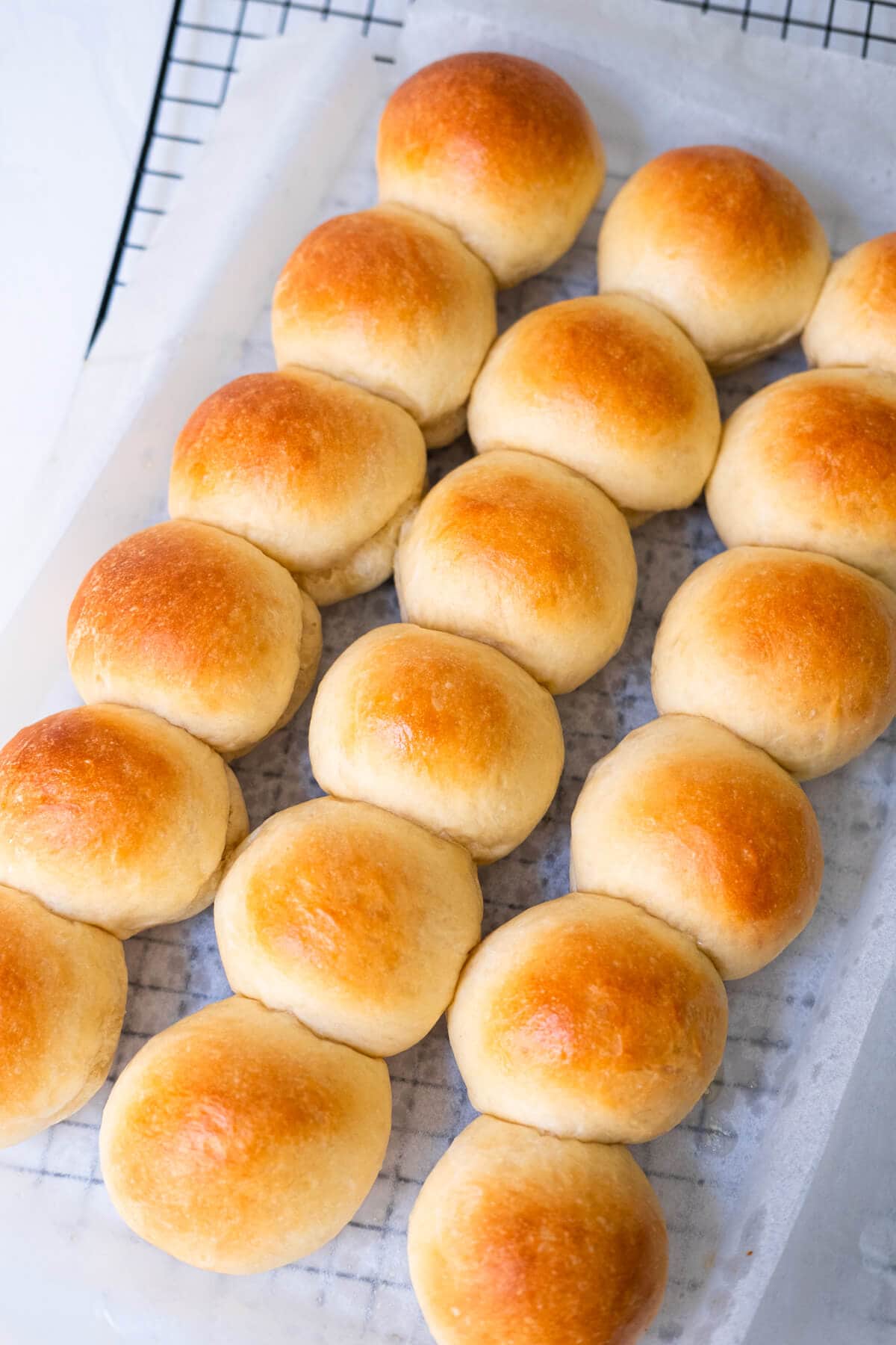 Slider buns on a wire rack lined with parchment paper.