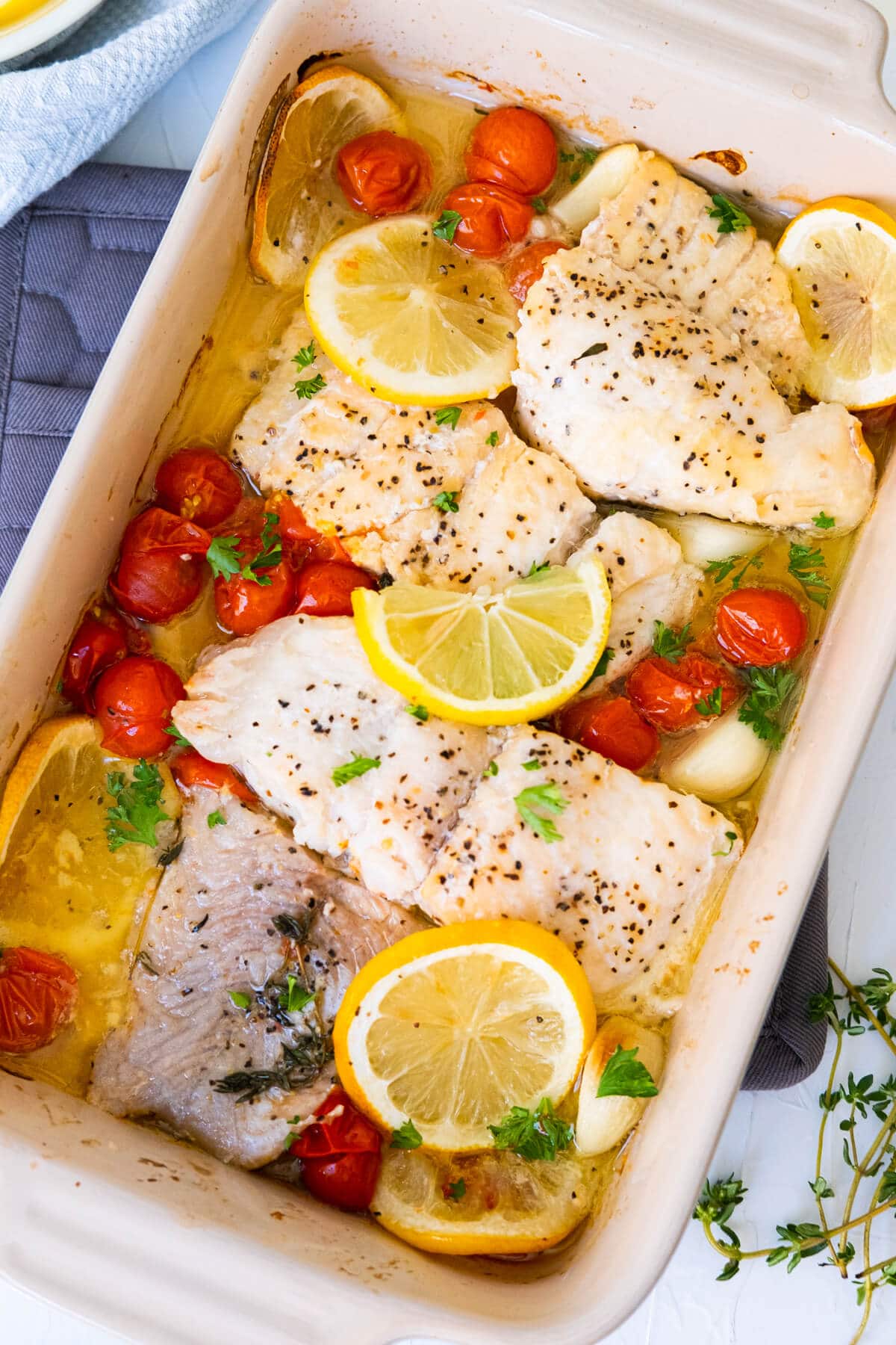 Baked catfish in a baking dish made with cherry tomatoes, lemon slices, garlic and thyme. 