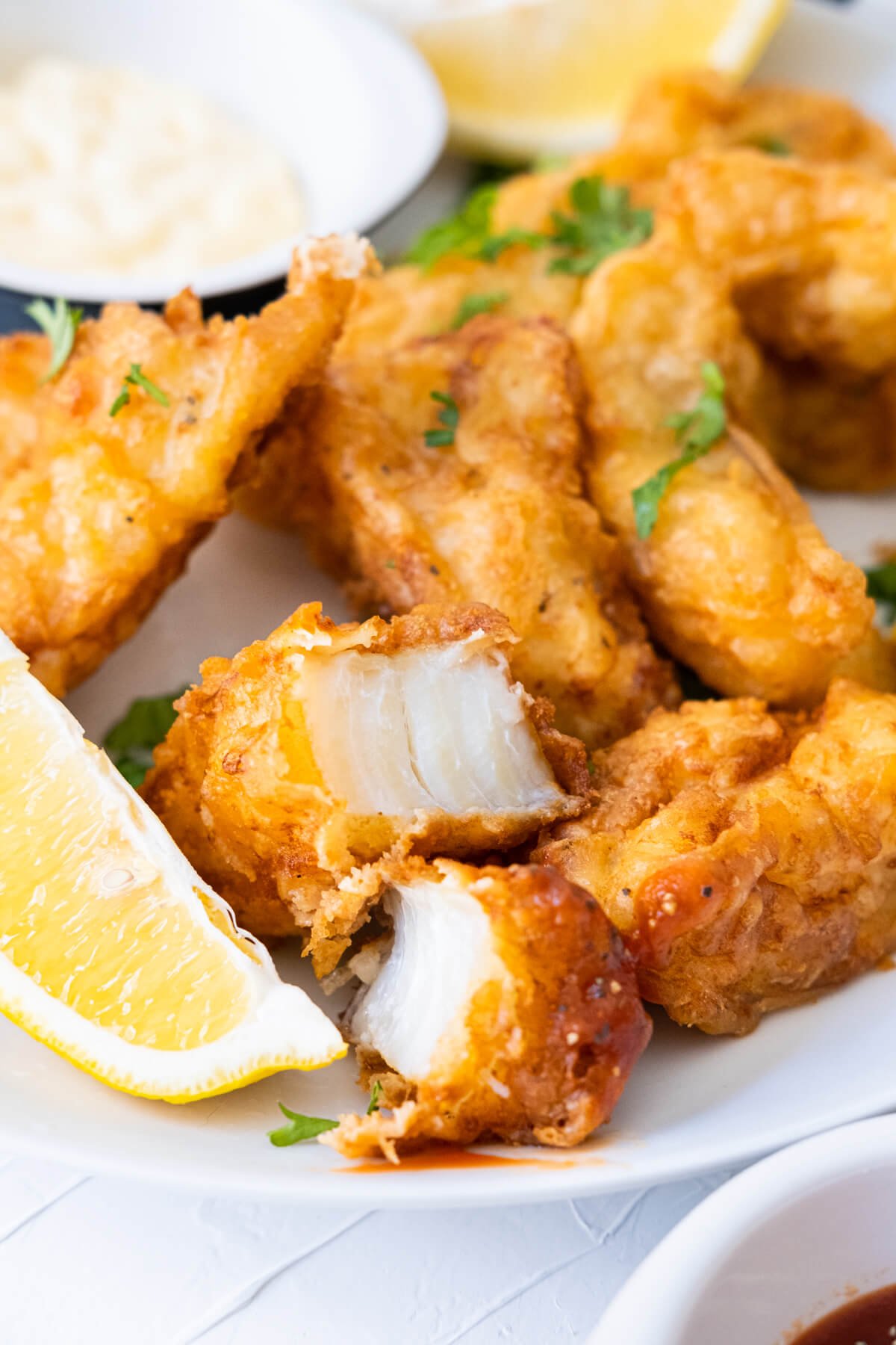 Tender, flaky beer-battered fish on a plate with lemon wedges and mayo. 