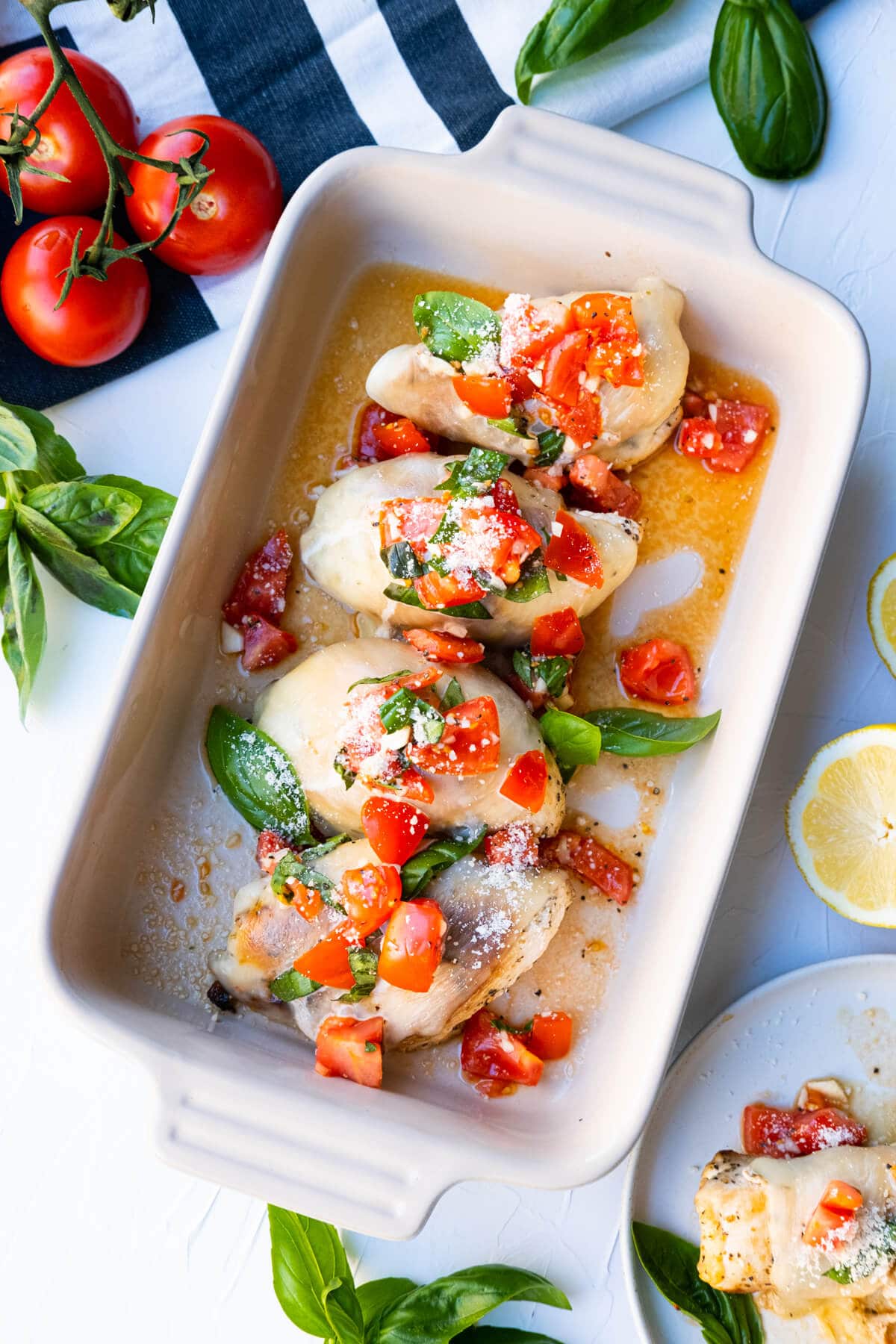 Bruschetta chicken served in a rectangle dish with fresh tomatoes, lemon and basil aside.