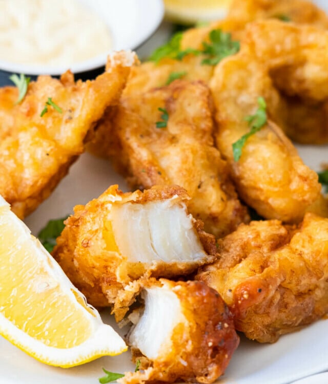 Tender, flaky beer-battered fish on a plate with lemon wedges and mayo.
