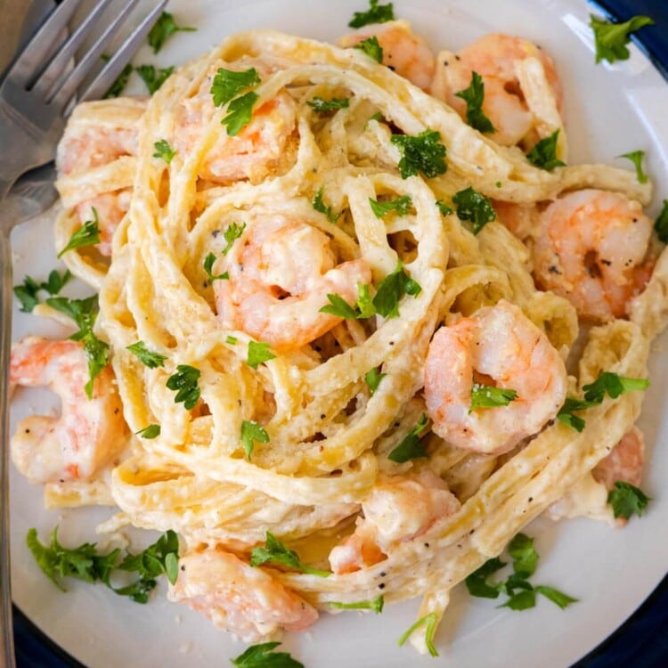 Shrimp fettuccine alfredo on a plate with freshly chopped parsley on top.