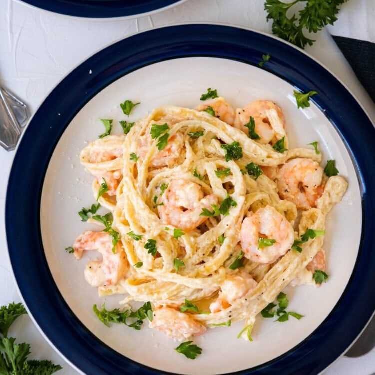 Creamy shrimp fettuccine alfredo served in the plate with freshly parsley aside.