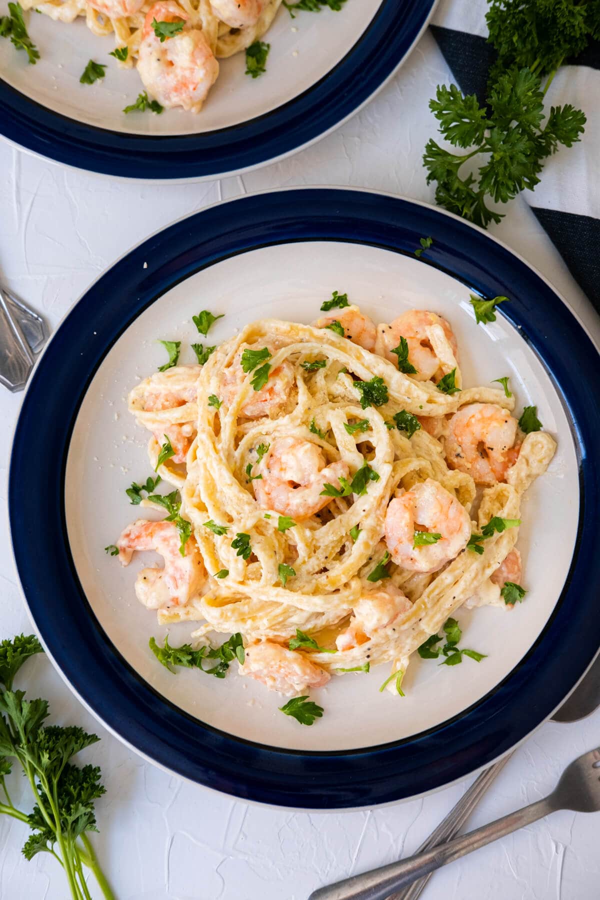 Creamy shrimp fettuccine alfredo served in the plate with freshly parsley aside. 