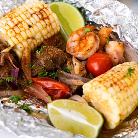 Surf'n Turf foil packs with steak, shrimp, tomatoes, corn and red onion sliced grilled.