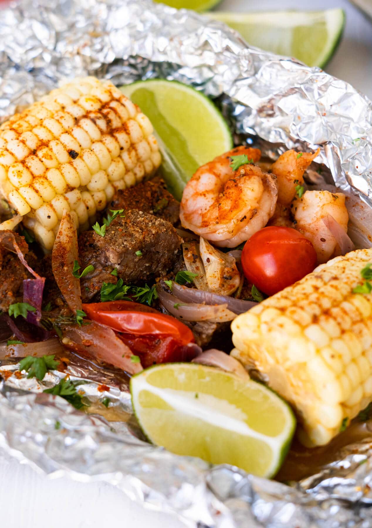 Grilled steak, shrimp, tomatoes, onion slices, corn with lime wedges and topped with chopped parsley on top.  