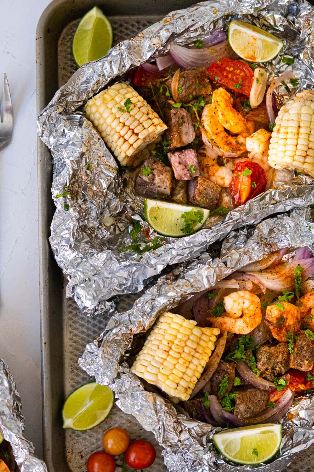 Grilled surf'n turf foil packs placed on a baking sheet. 