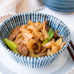Beef chow fun noodles with beef slices, green onion and bean sprouts in a blue strips bowl.