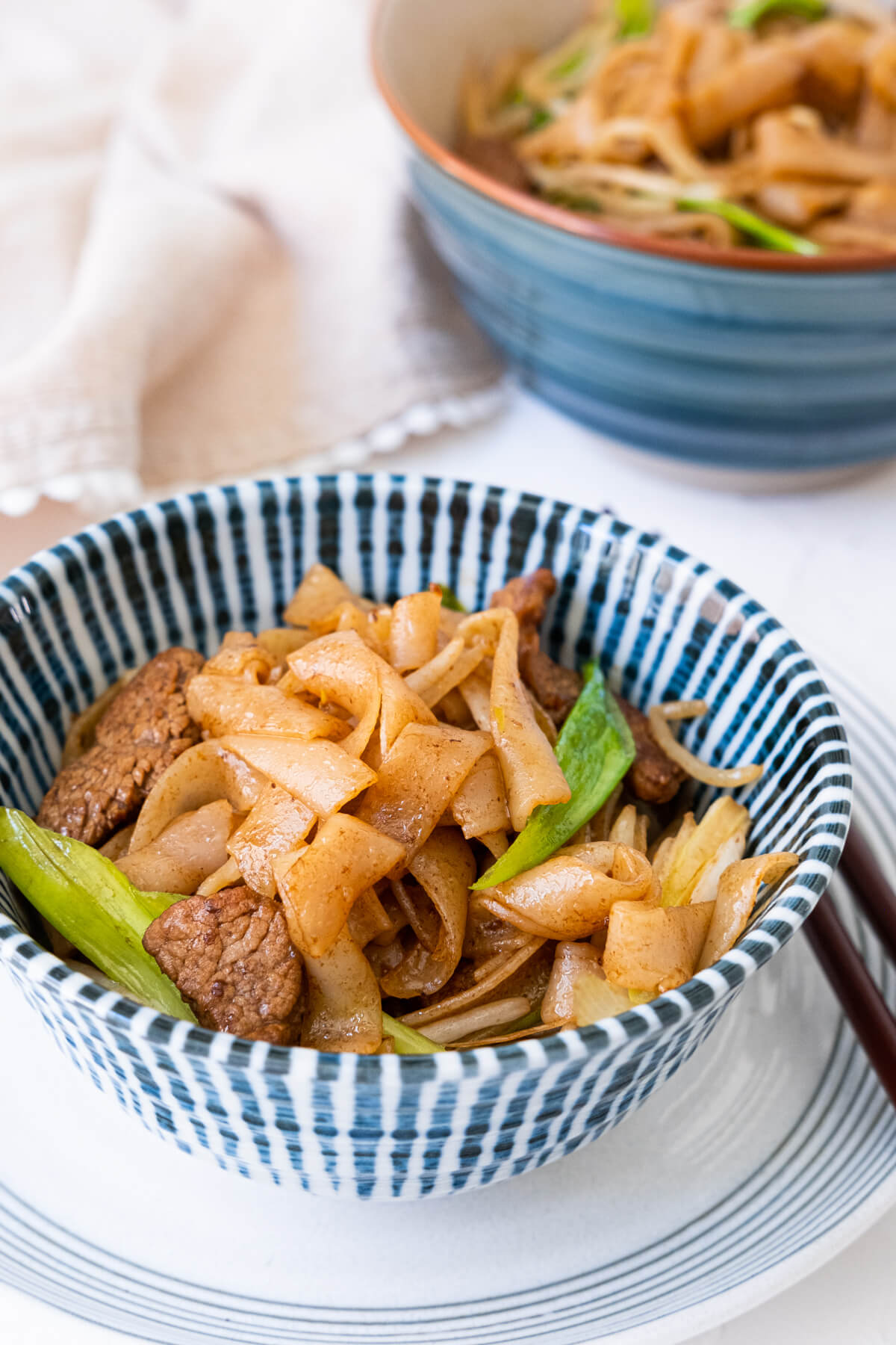 Two bowls of beef chow fun noodles placed on table and with the kitchen towel placed next to them.