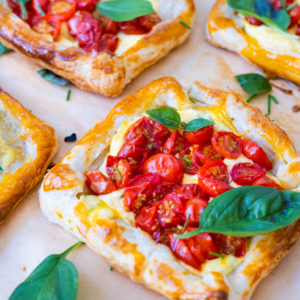 Savory cherry tomato tarts on parchment paper and topped with basil leaves.