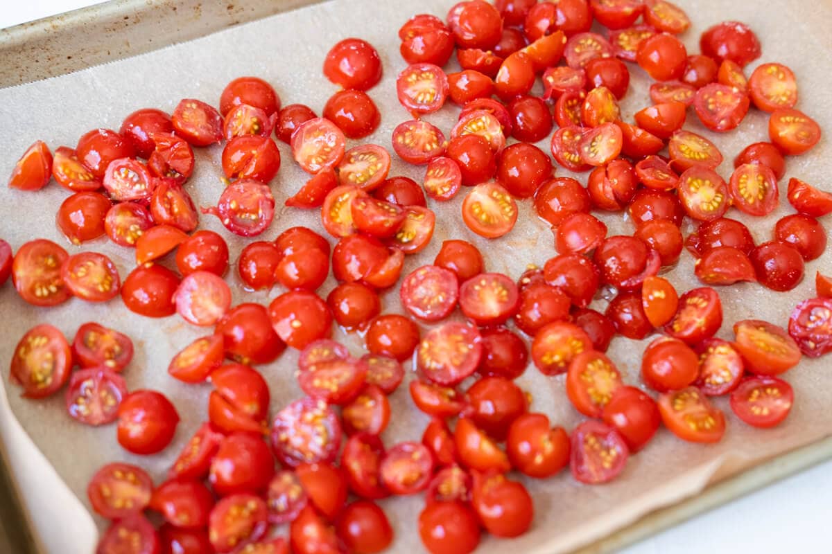 Cherry tomatoes sliced in half arranged on a baking tray lined with baking paper. 