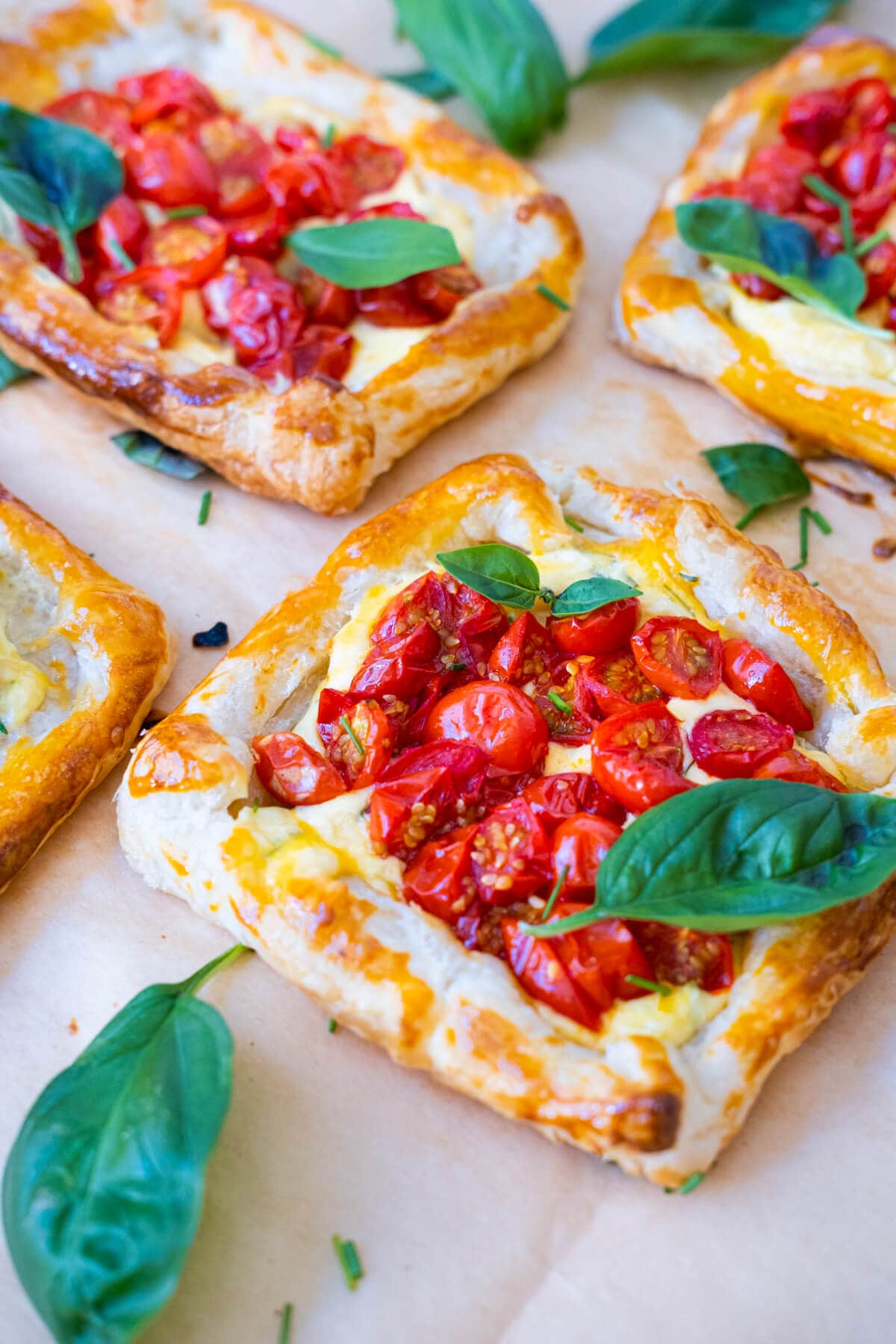 Savory tarts on parchment paper and topped with basil leaves and cherry tomatos.