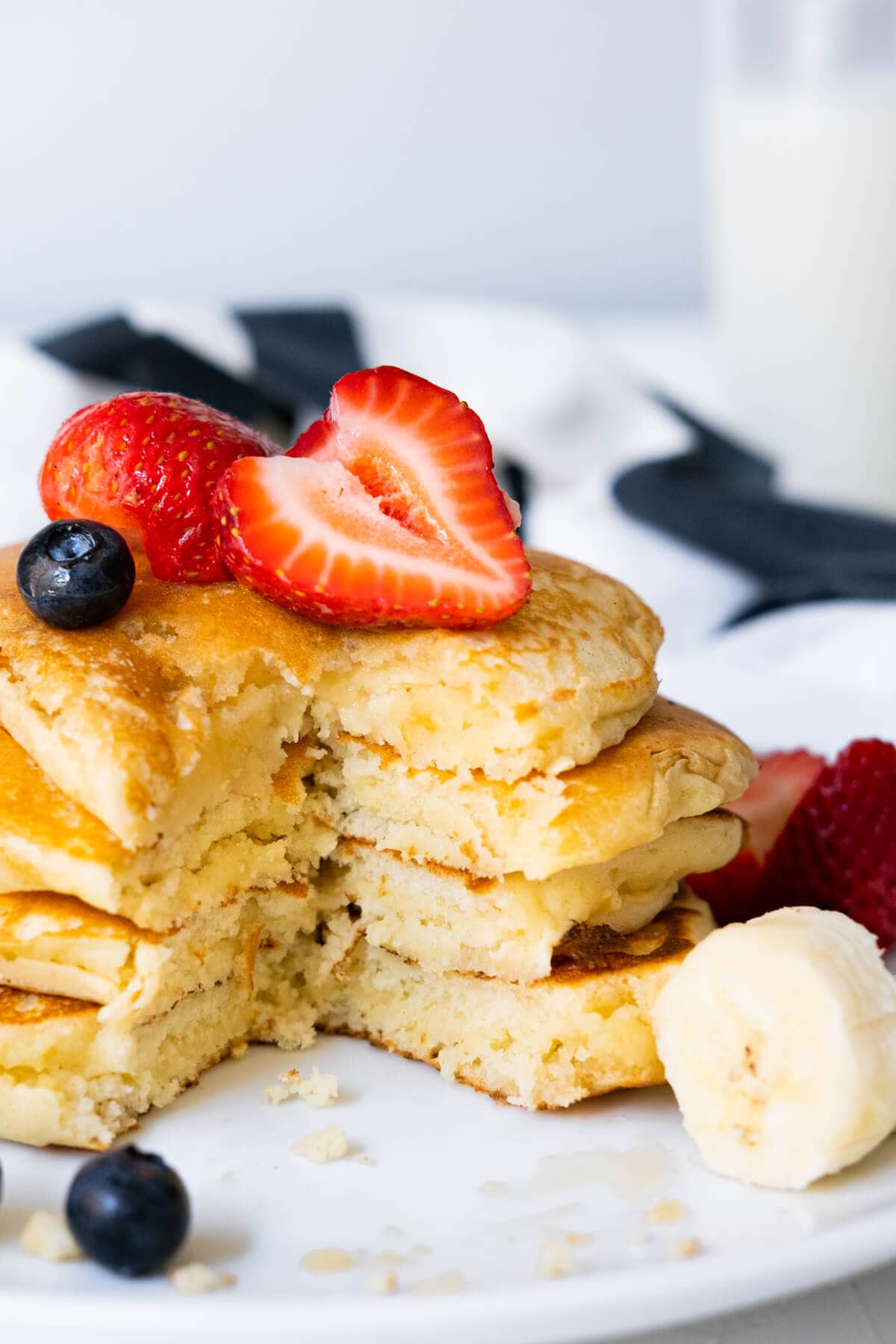 Pancakes stacked on each other with a cut in the center surrounded with strawberries, banana slices, and blueberries.