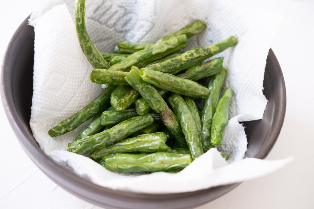 After deep-frying the green beans, remove them to a bowl lined with paper towel to and helps to drain the excess oil. 