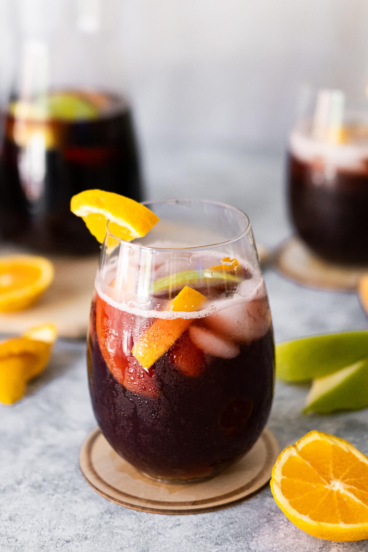 One large pitcher and two glasses of Spanish sangria on the table with orange slices placed aside. 