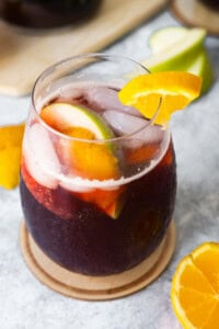 Spanish sangria in a glass with apple and orange slices aside.