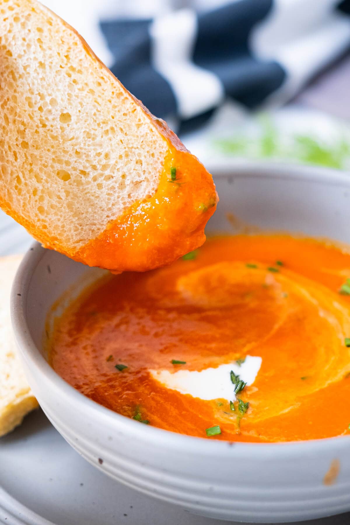 A slice of French bread dipped in a bowl of tomato soup. 