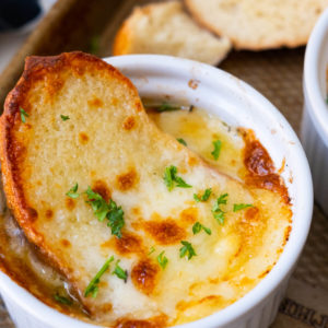 Golden brown broiled easy French onion soup served in a ramekin with two slices of bread aside.