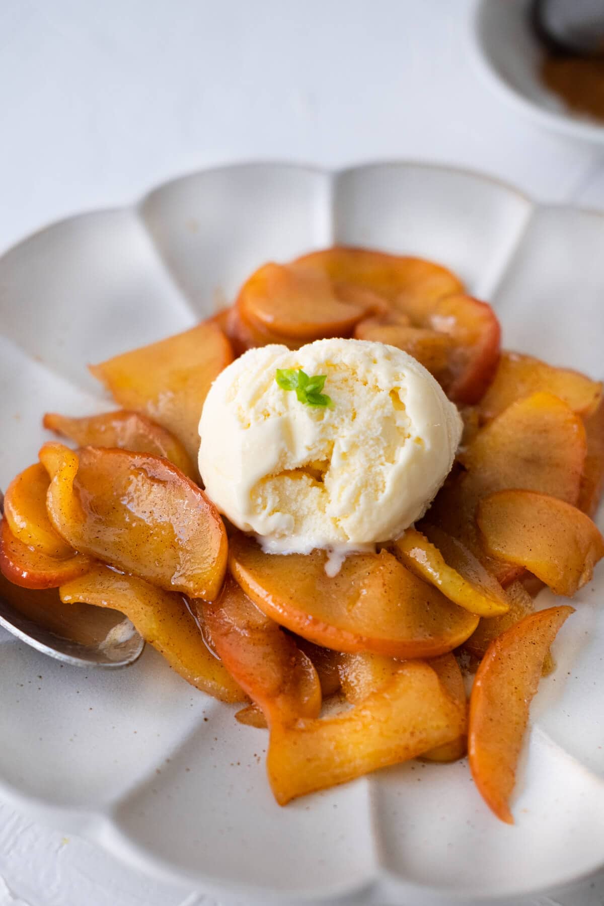 Golden brown fried apples slices with ice cream on top served in a white flower pattern plate.