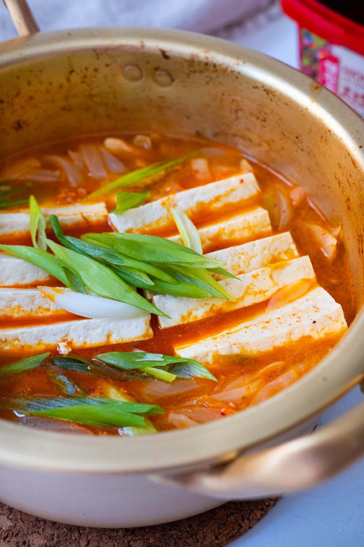 Easy kimchi jjigae in a pot with firm tofu, kimchi, pork belly and onion slices.