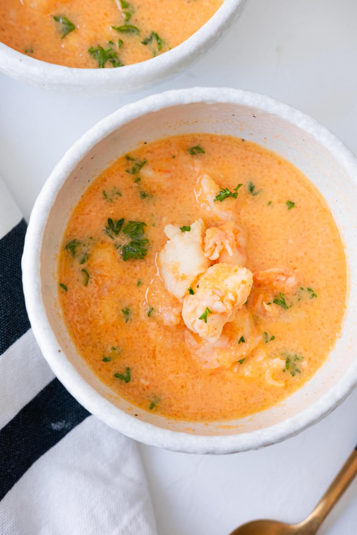 Shrimp bisque in a small white bowl with kitchen towel and a spoon placed aside.  