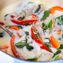 Spicy coconut chicken stew with red bell pepper, baby spinach leaves and fresh basil leaves on top.