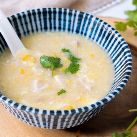 Sweet corn and chicken soup in a small bowl with cilantro leaves on top.