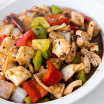Black bean sauce chicken in a white shallow bowl with red and green bell peppers..