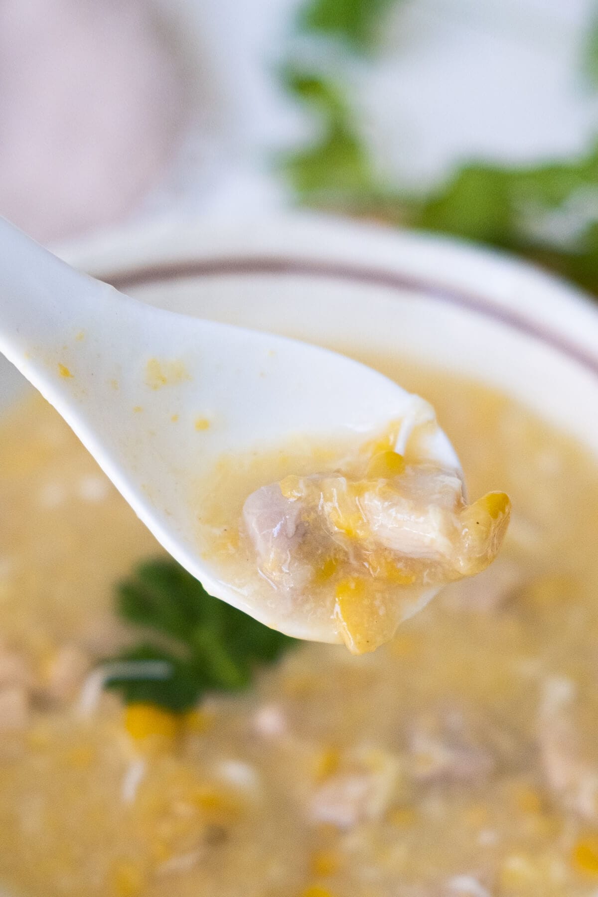 A spoon scooped some soup with some sweet corn and chicken. 