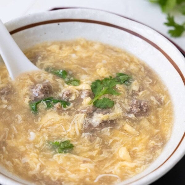 West lake beef soup with chopped coriander leaves on top and a black plate on the bottom.