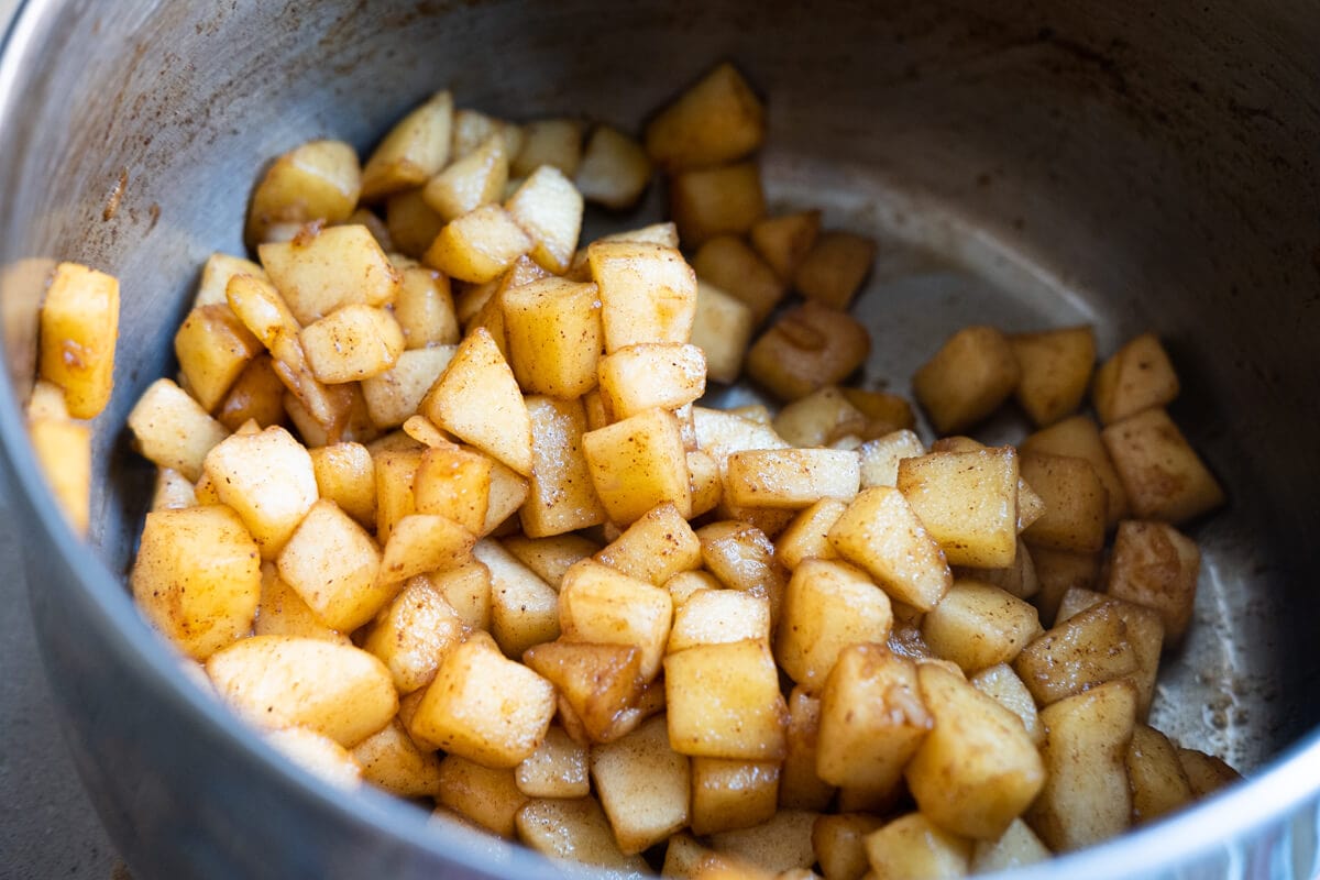 Melted brown sugar mixed well with apple bites and ground cinnamon in a pot.
