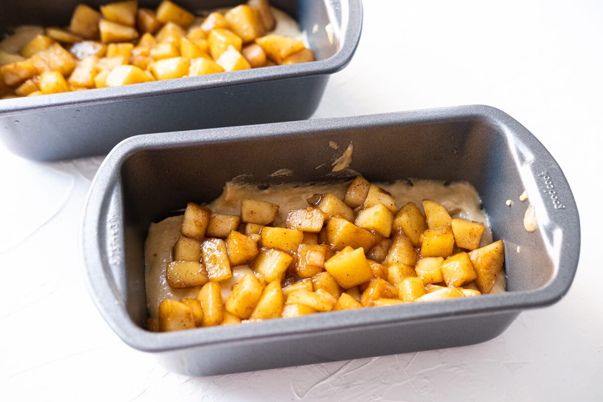 Batter transferred into two small loaf pans with apple pieces on top.