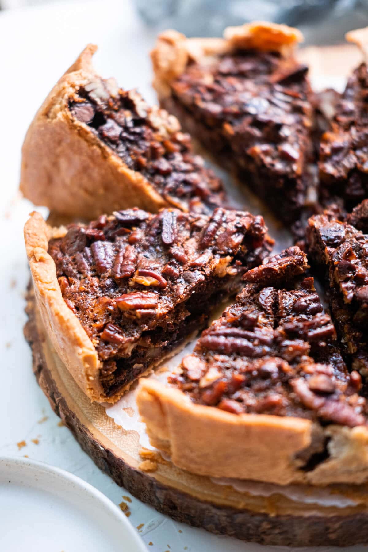 Delicious chocolate pecan pie sits on a wooden plate. 