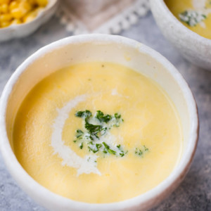 Japanese corn soup/ corn potage is served in a soup bowl is topped with finely chopped parsley and drizzled with heavy whipping cream.